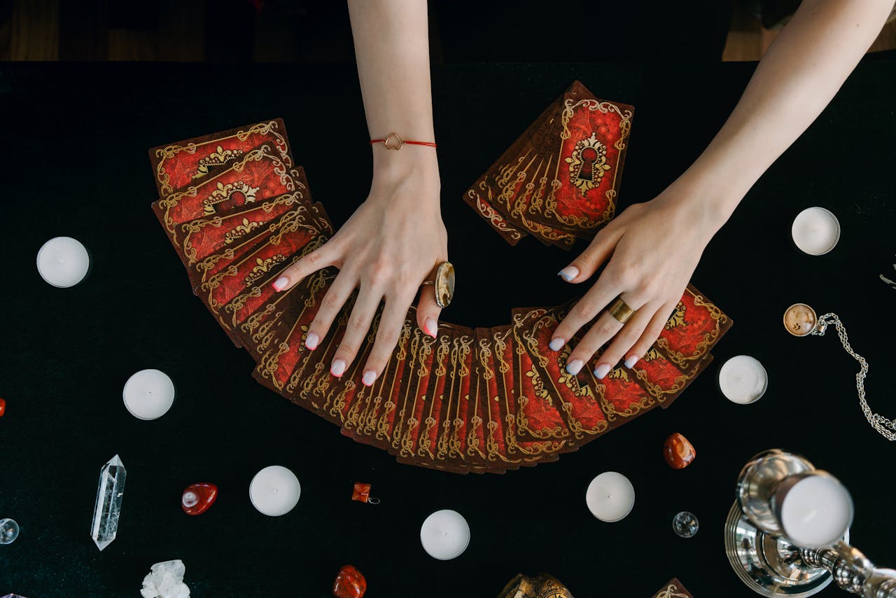 about-03 Hands arranging tarot cards on a table surrounded by candles and crystals, creating a mystical ambiance.
