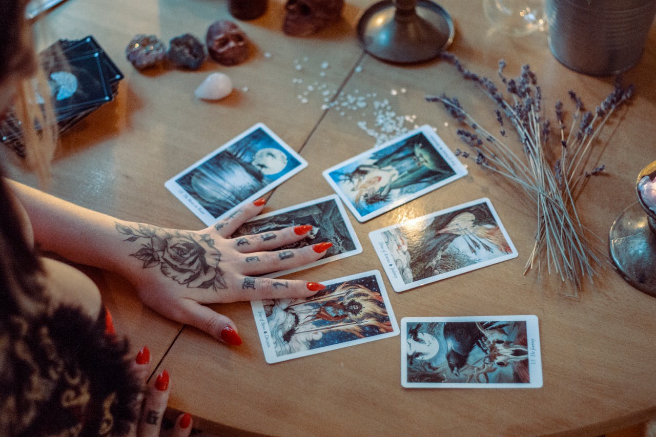 about-02 A mystical setup featuring tarot card reading on a wooden table, with artistic tattoos and dried flowers.